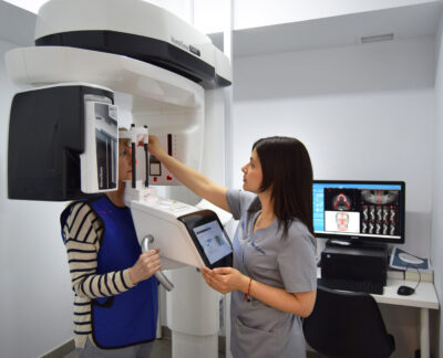 11Dentista vestida con uniforme clínico, ajusta la máquina para alinear correctamente la cabeza de la paciente. Imágenes radiológicas en la pantalla,